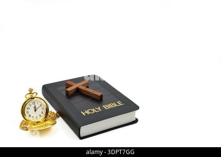 Pocket watch next to a black leather Holy Bible and a wooden cross on Bible with a white background. Copy space above and to the right side. Stock Photo