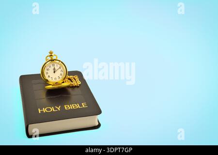 Pocket watch on a black leather Holy Bible with a light blue background. Copy space above and to the right side. Stock Photo