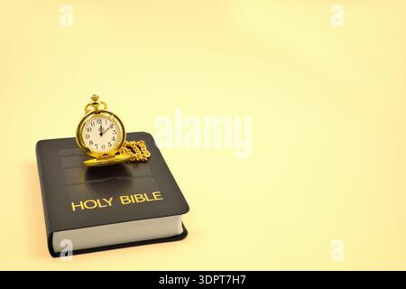 Pocket watch on a black leather Holy Bible with a warm yellow background. Copy space above and to the right side. Stock Photo