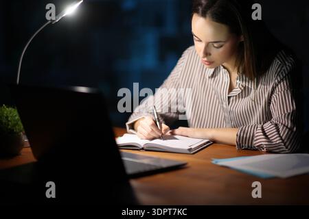 Self employed working in the night writing in agenda working at home Stock Photo