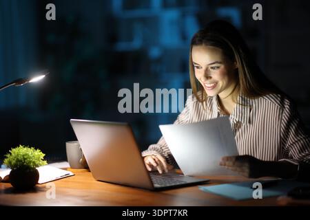 Happy self employed is working online holding documents in the night at home Stock Photo