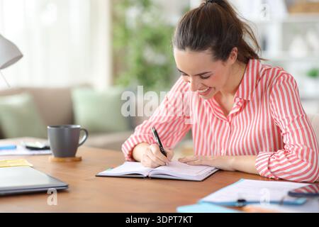 Happy self employed working writing ontes in agenda at home Stock Photo