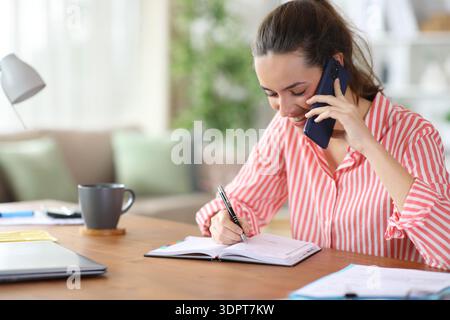 Happy self employed writing in agenda talking on phone working at home Stock Photo