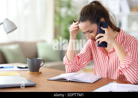 Worried freelance worker talking on phone checking agenda working at home Stock Photo
