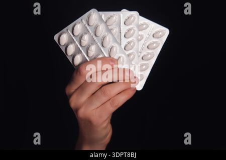 Womans hand holding a fan of medicine blister packs with white pills. Concept of treatment, healthcare, pharmacy, or overdose. Stock Photo