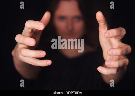 Woman with outstretcched hands on a dark background holding or grabbing an imaginary object or interacting with virtual reality and technology. Stock Photo