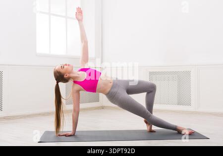 Young Woman Performs Side Plank Pose on Yoga Mat in Bright Studio During Daytime Stock Photo