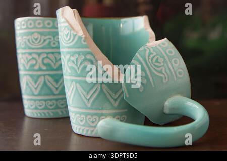 Broken turquoise ceramic cup with handle pieces on wooden table surface Stock Photo