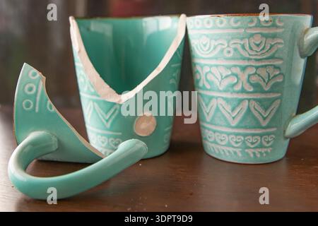 Broken turquoise ceramic cup with handle pieces on wooden table surface Stock Photo