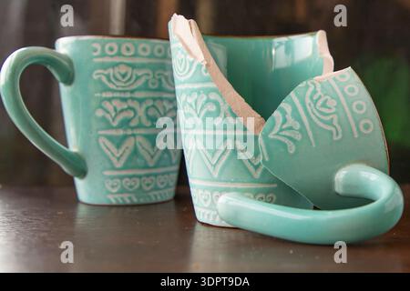 Broken turquoise ceramic cup with handle pieces on wooden table surface Stock Photo