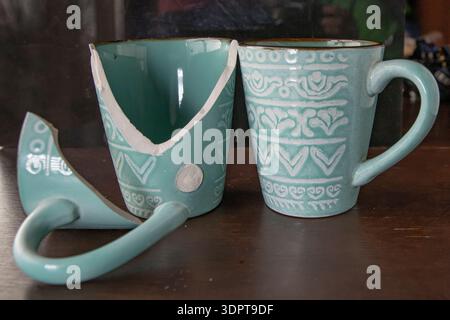 Broken turquoise ceramic cup with handle pieces on wooden table surface Stock Photo