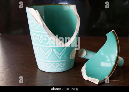 Broken turquoise ceramic cup with handle pieces on wooden table surface Stock Photo