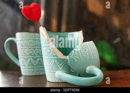 Broken turquoise ceramic cup with red heart decoration on wooden table Stock Photo