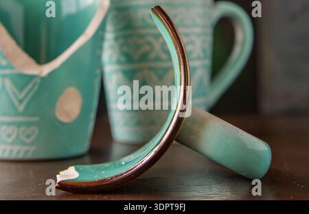 Broken turquoise ceramic cup with handle pieces on wooden table surface Stock Photo