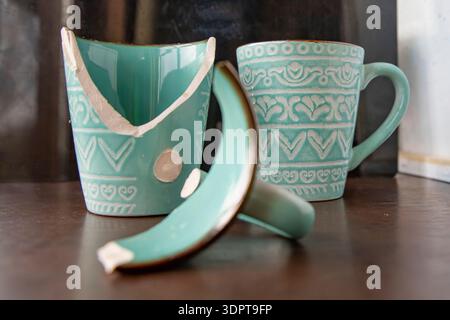 Broken turquoise ceramic cup with handle pieces on wooden table surface Stock Photo
