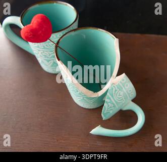Broken turquoise ceramic cup with red heart decoration on wooden table Stock Photo