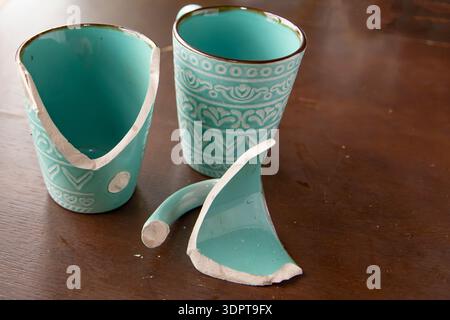 Broken turquoise ceramic cup with handle pieces on wooden table surface Stock Photo