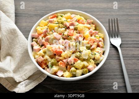 Olivier salad from boiled vegetables, dressed with mayonnaise sauce in bowl on wooden background.  Traditional russian salad. Close up view Stock Photo