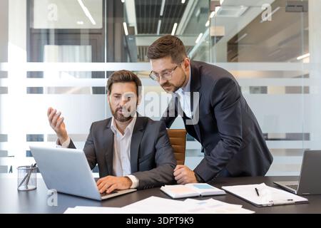 Two professional businessmen are collaborating and discussing business strategy, working together on a laptop during an informal meeting in a contemporary office setting Stock Photo