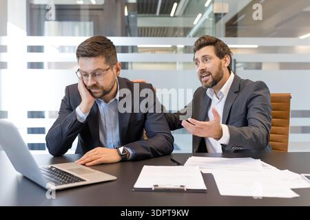Upset businessman in a suit having a conversation with a colleague reassuring him, showing support and empathy for his burnout and stress in a modern office meeting room Stock Photo