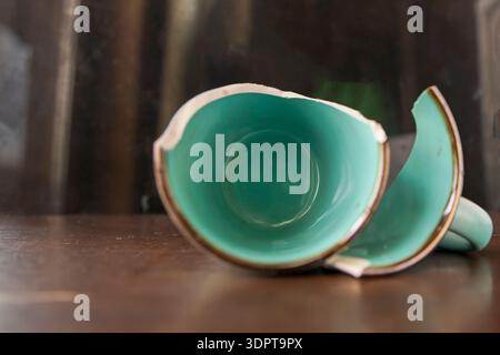 Broken turquoise ceramic cup with handle pieces on wooden table surface Stock Photo