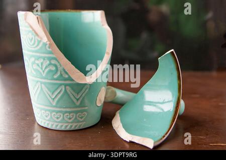 Broken turquoise ceramic cup with handle pieces on wooden table surface Stock Photo