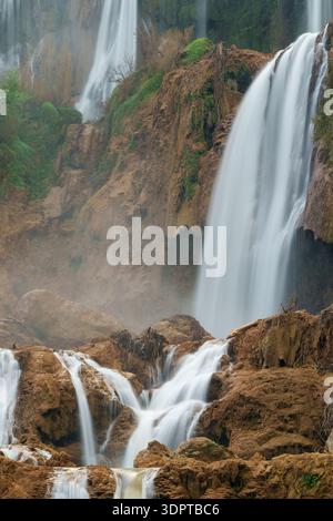Multi-level waterfall cascades flow over limestone rock formations, with mist rising from the falling water. Stock Photo