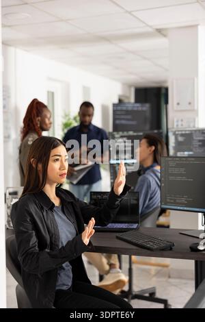 Asian female programmer works with 3D interface in modern office, testing code for app development. Woman doing hand gestures while interacting with holographic screen, analyzing website performance. Stock Photo