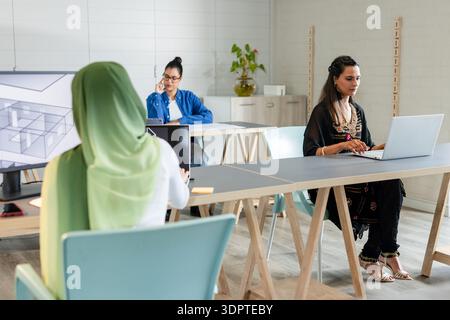 Diverse female coworkers working on design projects at desks in coworking office with monitors Stock Photo