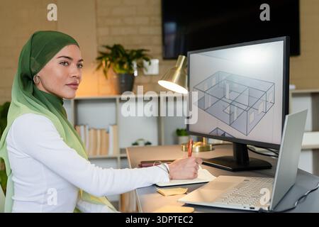 Asian Indian woman holding pen studying 3D floor plan on monitor at office desk, copy space Stock Photo