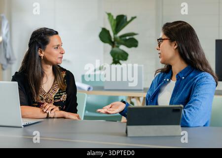 Diverse female colleagues discussing project over laptop tablet and document at modern office table Stock Photo