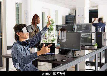 Asian software developer wears VR glasses and interacts with virtual 3D programming environment. The scene highlights cutting edge technology, coding analysis and innovation in software development. Stock Photo