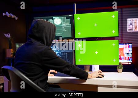 Hooded hacker using isolated screen PC to steal credit card numbers and infiltrate banking systems. Rogue programmer in secret hideout running malicious code on mockup computer displays Stock Photo