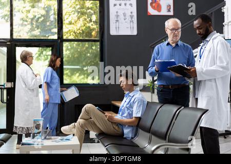 African american physician stands beside male patient discussing treatment options in modern clinic lobby. Medical conversation highlights teamwork, professionalism and attentive patient care. Stock Photo