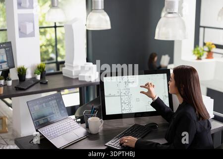 Asian woman focuses on drafting architectural layouts, developing house plans and assessing structural needs. Skilled architect edits digital designs and prepares detailed presentation for contractor. Stock Photo