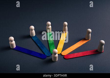 Seven wooden figures arranged in a circular formation on different colored wooden sticks over a dark background. Concept of business leadership, team Stock Photo