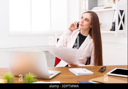 Business Professional Speaks on the Phone While Reviewing Documents in a Modern Office Space Stock Photo