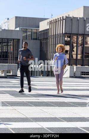 African American couple jogging on patterned pavers at plaza, wearing athletic clothing and watch Stock Photo