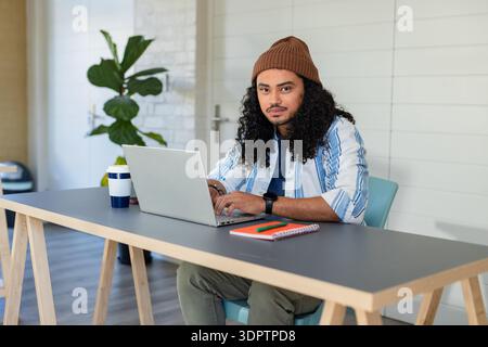 Man typing on laptop at home office desk with reusable coffee cup, notebook and colored pens Stock Photo