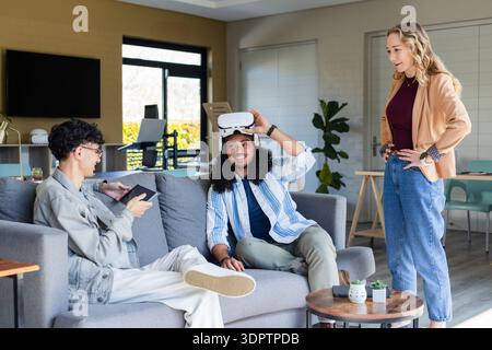 Diverse coworkers testing virtual reality headset together at office lounge with tablet smartphone Stock Photo