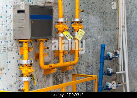 Yellow gas pipes with valves and meters mounted on tiled wall near industrial utility box Stock Photo