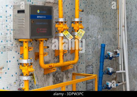 Yellow gas pipes with valves and control box mounted on tiled wall in industrial or utility setting Stock Photo