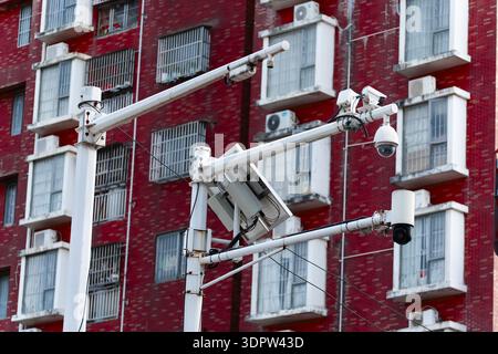 Security cameras mounted on poles in front of red brick residential building with air conditioning units and barred windows Stock Photo