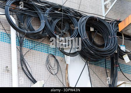 Coiled black electrical cables hanging on tiled wall with blue mosaic border, urban infrastructure detail Stock Photo