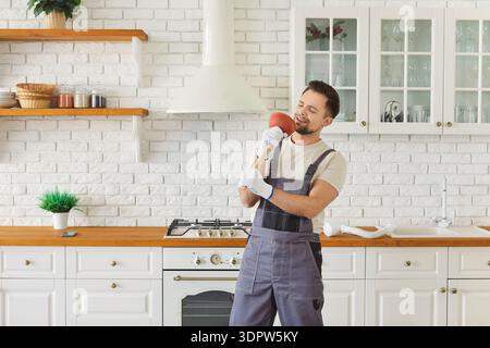 Plumber holding plunger like microphone and singing in modern kitchen Stock Photo