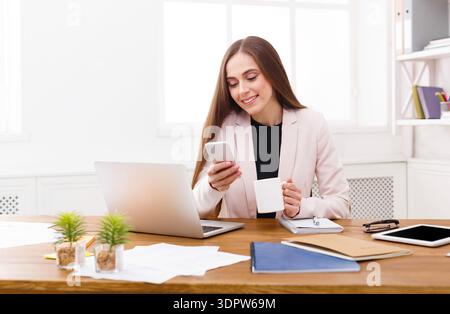 Woman Sits at Desk Using Smartphone and Holding Cup in Modern Office Space During Daytime Stock Photo