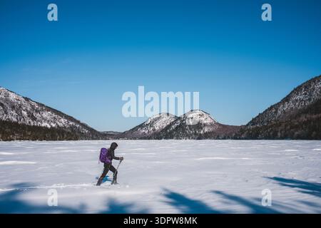 Female hikes across frozen Jordan Pond in Acadia on frigid winter day. Stock Photo