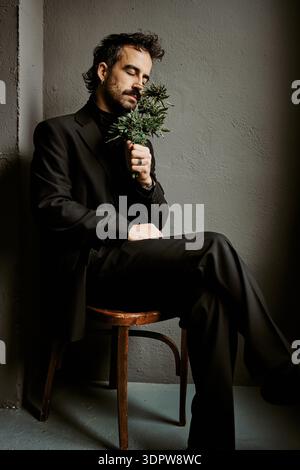 Elegant man in suit smelling fresh cannabis plant in dark studio Stock Photo