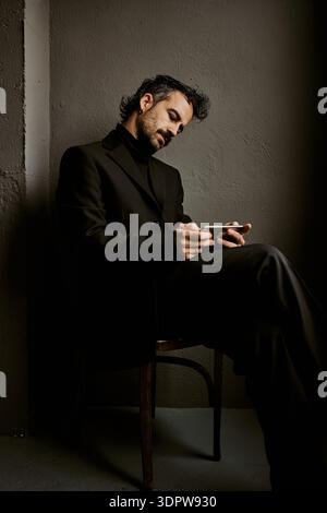 Elegant man in black suit using smartphone in dark studio Stock Photo