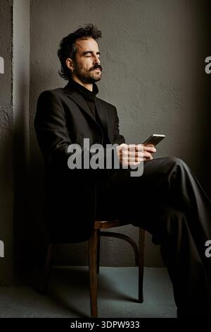 Elegant man in black suit using smartphone in dark studio Stock Photo
